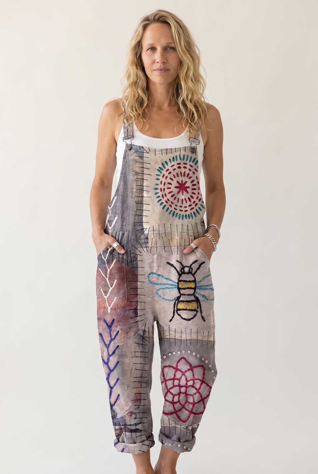 A woman modeling a sleeveless patchwork-print overall jumpsuit with a bee and floral design, set against a plain light background.