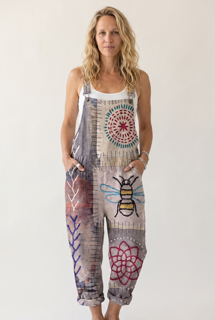 A woman modeling a sleeveless patchwork-print overall jumpsuit with a bee and floral design, set against a plain light background.